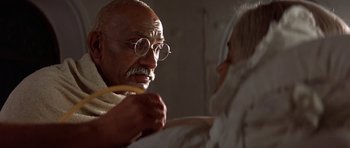 Movie still from “Gandhi” (1982), directed by Richard Attenborough – An old man wearing glasses and holding a banana; Close Up shot, Over the shoulder angle