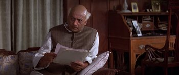 Movie still from “Gandhi” (1982), directed by Richard Attenborough – An older man sitting in a chair holding papers; Close Up shot, High angle