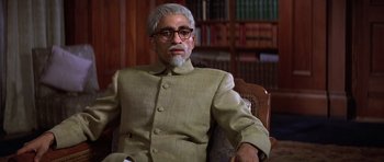 Movie still from “Gandhi” (1982), directed by Richard Attenborough – An older man sitting in a chair in a room; Medium shot, Low angle