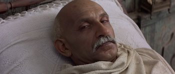 Movie still from “Gandhi” (1982), directed by Richard Attenborough – An older man with a mustache is laying in bed; Close Up shot, High angle