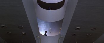 Movie still from “Gattaca” (1997), directed by Andrew Niccol – A man standing inside of a building looking up at the ceiling; Extreme Wide shot, Overhead angle