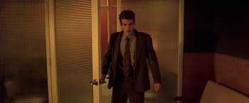 Movie still from “Gattaca” (1997), directed by Andrew Niccol – A man in a suit and tie standing in front of an open door; Medium shot, Low angle