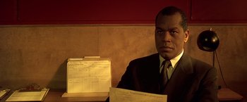 Movie still from “Gattaca” (1997), directed by Andrew Niccol – A man sitting in front of a bunch of papers; Close Up shot, Low angle