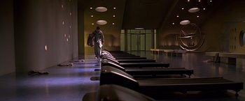 Movie still from “Gattaca” (1997), directed by Andrew Niccol – A man is walking through a row of benches in a gym; Wide shot, Low angle