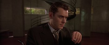 Movie still from “Gattaca” (1997), directed by Andrew Niccol – A man in a suit and tie sitting in front of a spiral staircase; Close Up shot, Low angle