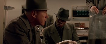 Movie still from “Gattaca” (1997), directed by Andrew Niccol – Two men in suits and hats are looking at a piece of paper on a table; Close Up shot, Over the shoulder angle
