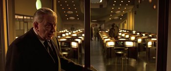 Movie still from “Gattaca” (1997), directed by Andrew Niccol – A man standing in front of a room full of tables; Medium shot, High angle