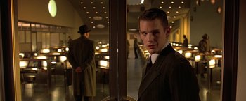 Movie still from “Gattaca” (1997), directed by Andrew Niccol – A man in a suit standing in front of two other men; Close Up shot, Low angle
