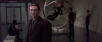 Movie still from “Gattaca” (1997), directed by Andrew Niccol – A man standing in front of two other men; Medium shot, Over the shoulder angle