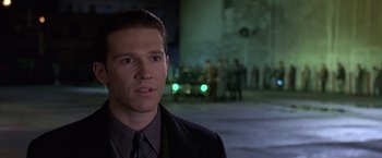 Movie still from “Gattaca” (1997), directed by Andrew Niccol – A man wearing a suit and tie standing in front of a building; Close Up shot, Over the shoulder angle