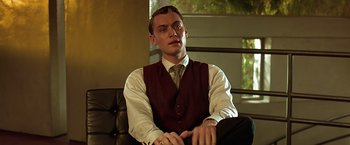 Movie still from “Gattaca” (1997), directed by Andrew Niccol – A man sitting on top of a couch wearing a vest; Medium shot, Low angle
