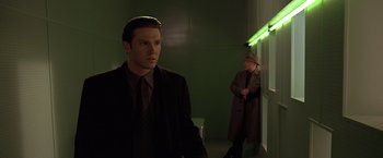 Movie still from “Gattaca” (1997), directed by Andrew Niccol – A man in a suit and tie standing next to another man in a coat and hat; Medium shot, Over the shoulder angle
