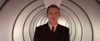 Movie still from “Gattaca” (1997), directed by Andrew Niccol – A man wearing a suit and tie standing in front of a wall; Close Up shot, Low angle