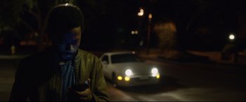 Movie still from “Get Out” (2017), directed by Jordan Peele – A man is looking at his cell phone while standing on the side of the road; Close Up shot, Low angle
