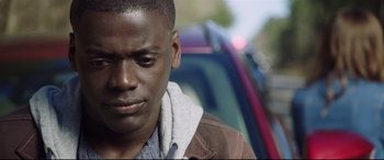 Movie still from “Get Out” (2017), directed by Jordan Peele – A person with a car in the background; Close Up shot, Over the shoulder angle