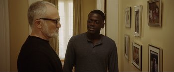Movie still from “Get Out” (2017), directed by Jordan Peele – A man standing next to another man in front of a window; Medium shot, Over the shoulder angle