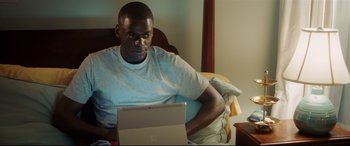 Movie still from “Get Out” (2017), directed by Jordan Peele – A man sitting in a bed looking at a laptop computer; Medium shot, High angle