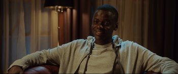 Movie still from “Get Out” (2017), directed by Jordan Peele – A man in a grey hoodie smiling for the camera; Medium shot, Over the shoulder angle
