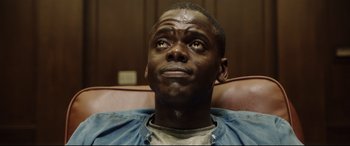 Movie still from “Get Out” (2017), directed by Jordan Peele – A person sitting in a chair looking up; Close Up shot, Low angle