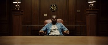 Movie still from “Get Out” (2017), directed by Jordan Peele – A man sitting in a chair in front of a dartboard; Medium shot, Low angle
