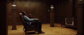 Movie still from “Get Out” (2017), directed by Jordan Peele – A man sitting in a chair next to a podium; Wide shot, High angle