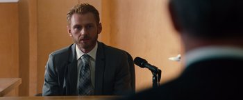 Movie still from “Gifted” (2017), directed by Marc Webb – A man wearing a suit and tie sitting in front of a microphone; Close Up shot, Over the shoulder angle