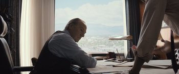 Movie still from “Gold” (2016), directed by Stephen Gaghan – An older man sitting at a desk in front of a window; Medium shot, Low angle