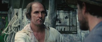Movie still from “Gold” (2016), directed by Stephen Gaghan – A person wearing a shirt with a bird cage in the background; Close Up shot, Low angle