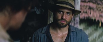 Movie still from “Gold” (2016), directed by Stephen Gaghan – A man with a hat and beard looking at the camera; Close Up shot, Over the shoulder angle