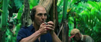 Movie still from “Gold” (2016), directed by Stephen Gaghan – A man smoking a cigarette in front of some trees; Close Up shot, Over the shoulder angle