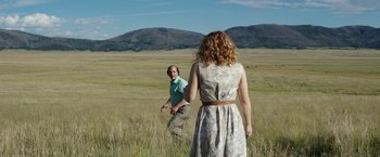 Movie still from “Gold” (2016), directed by Stephen Gaghan – A man and a woman are standing in a grassy field; Wide shot, Over the shoulder angle