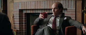 Movie still from “Gold” (2016), directed by Stephen Gaghan – A man sitting in a chair holding a coffee mug; Medium shot, Over the shoulder angle