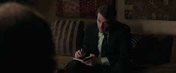 Movie still from “Gold” (2016), directed by Stephen Gaghan – A man in a suit writing in a notebook; Medium shot, Over the shoulder angle