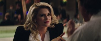 Movie still from “Gold” (2016), directed by Stephen Gaghan – A beautiful blonde woman with a white shirt and a black jacket; Close Up shot, Over the shoulder angle