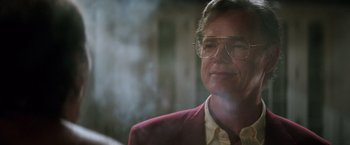 Movie still from “Gold” (2016), directed by Stephen Gaghan – A person wearing a suit and glasses; Close Up shot, Low angle