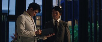 Movie still from “Gold” (2016), directed by Stephen Gaghan – A man in a suit and tie holding a tablet; Medium shot, Over the shoulder angle