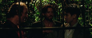 Movie still from “Gold” (2016), directed by Stephen Gaghan – A man with long hair and a beard standing next to trees; Medium shot, Over the shoulder angle