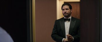 Movie still from “Gold” (2016), directed by Stephen Gaghan – A man in a tuxedo standing next to a wall; Medium shot, Over the shoulder angle