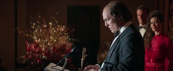 Movie still from “Gold” (2016), directed by Stephen Gaghan – A man standing at a podium holding a microphone; Close Up shot, Low angle