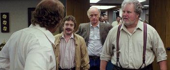 Movie still from “Gold” (2016), directed by Stephen Gaghan – A group of men standing next to each other in a room; Medium shot, Over the shoulder angle