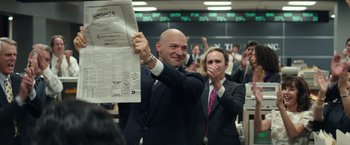 Movie still from “Gold” (2016), directed by Stephen Gaghan – A man in a suit and tie holding up a newspaper; Medium shot, Low angle