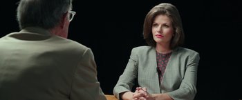 Movie still from “Gold” (2016), directed by Stephen Gaghan – A woman sitting in front of a man in front of a black background; Medium shot, Over the shoulder angle
