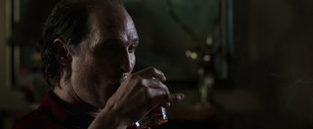 Movie still from “Gold” (2016), directed by Stephen Gaghan – A person holding a drink in his hand; Close Up shot, Over the shoulder angle