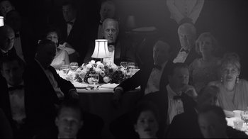Movie still from “Good Night, and Good Luck.” (2005), directed by George Clooney – A black and white photo of a group of people sitting at a dinner table; Medium shot, Over the shoulder angle