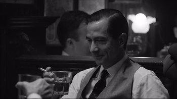Movie still from “Good Night, and Good Luck.” (2005), directed by George Clooney – A black and white photo of a man holding a glass of water; Close Up shot, Over the shoulder angle
