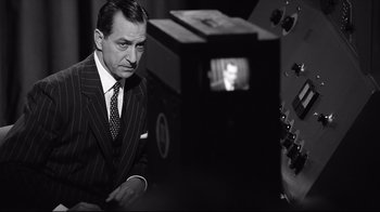 Movie still from “Good Night, and Good Luck.” (2005), directed by George Clooney – A man in a suit and tie in front of a television; Medium shot, Over the shoulder angle