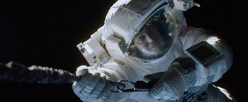 Movie still from “Gravity” (2013), directed by Alfonso Cuarón – A man in a spacesuit is holding something in his hand; Medium shot, Overhead angle