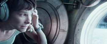 Movie still from “Gravity” (2013), directed by Alfonso Cuarón – A woman is talking on a cell phone in front of a round object; Close Up shot, High angle