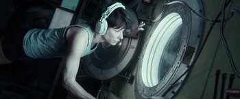 Movie still from “Gravity” (2013), directed by Alfonso Cuarón – A woman wearing headphones looking into a window; Medium shot, Overhead angle