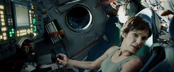 Movie still from “Gravity” (2013), directed by Alfonso Cuarón – A woman holding a camera in a room with books; Medium shot, Overhead angle